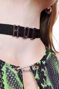 Close-up of a black webbing choker with silver "HOE" lettering. The adjustable design and bold statement print make it a perfect accessory for those who want to stand out with attitude.