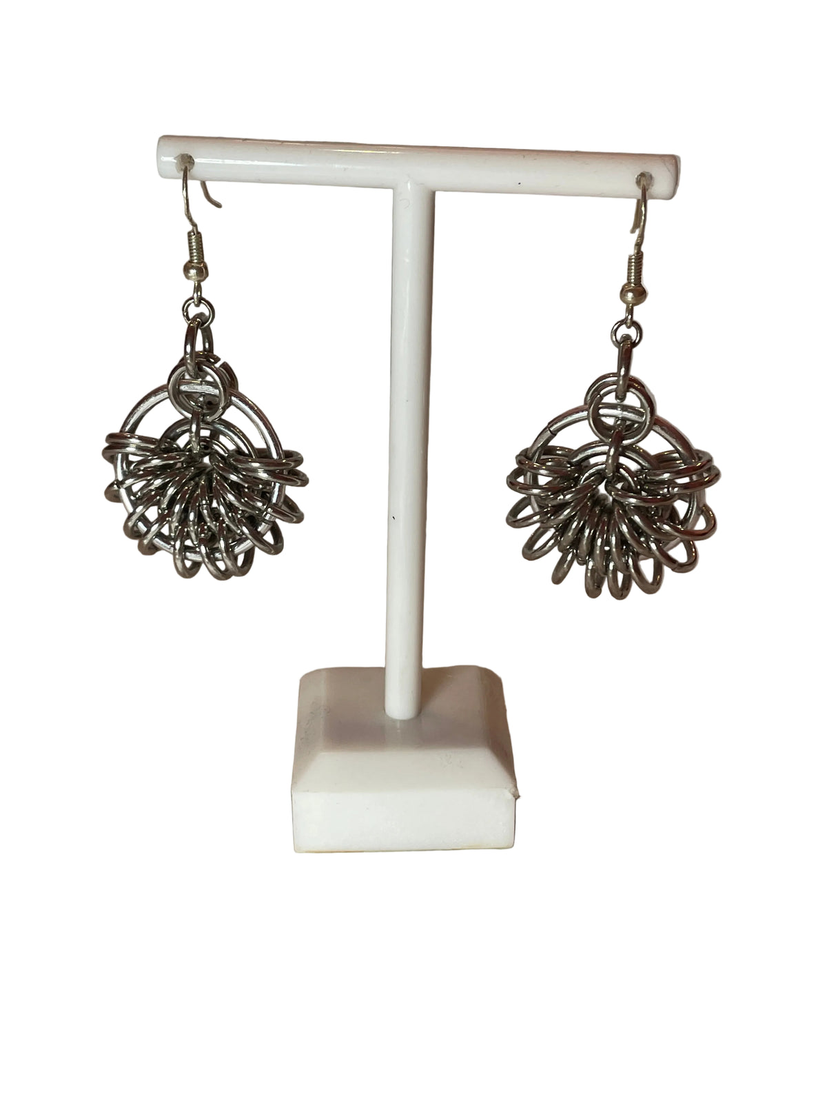 A detailed shot of round silver chain mail earrings, showcasing their unique and intricate design. The earrings hang elegantly, catching the light against a simple, neutral background.