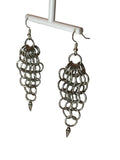 A close-up of chunky silver chain mail earrings with a bold, intricate weave. The earrings catch the light, showcasing their statement-making design against a minimalist background.
