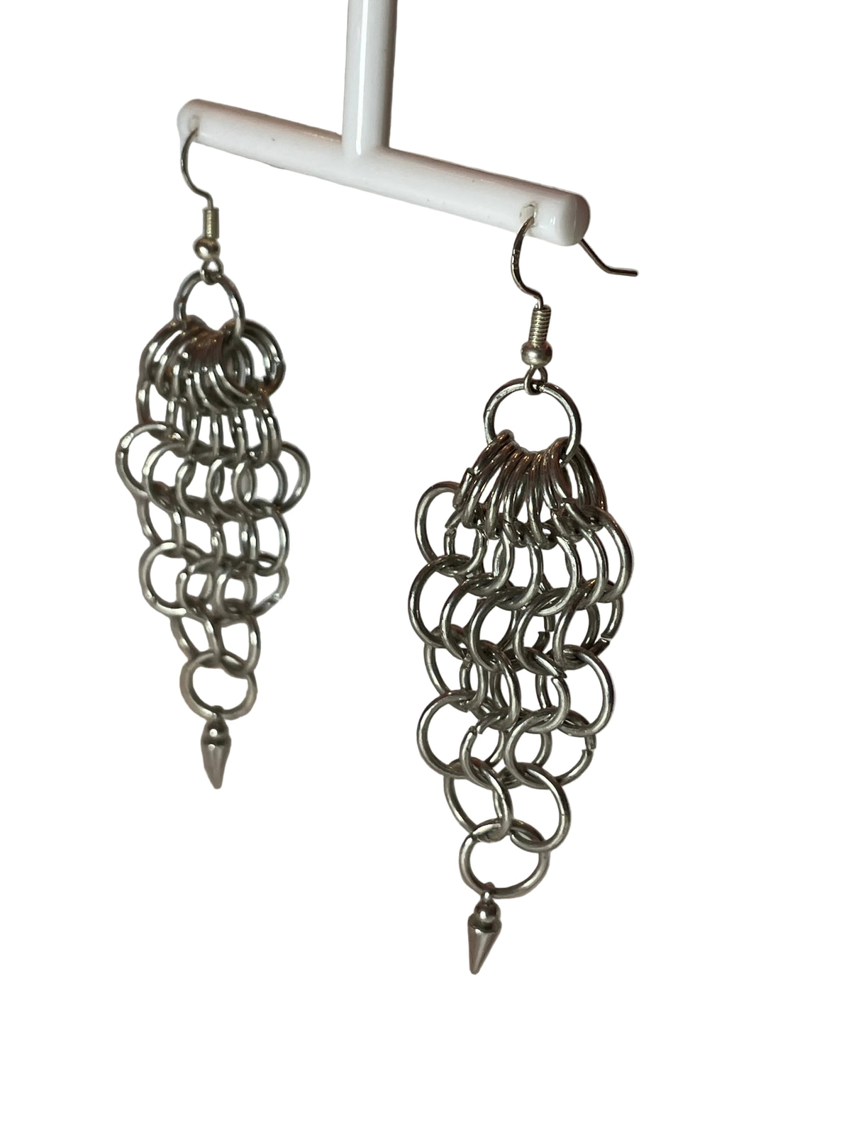 A close-up of chunky silver chain mail earrings with a bold, intricate weave. The earrings catch the light, showcasing their statement-making design against a minimalist background.