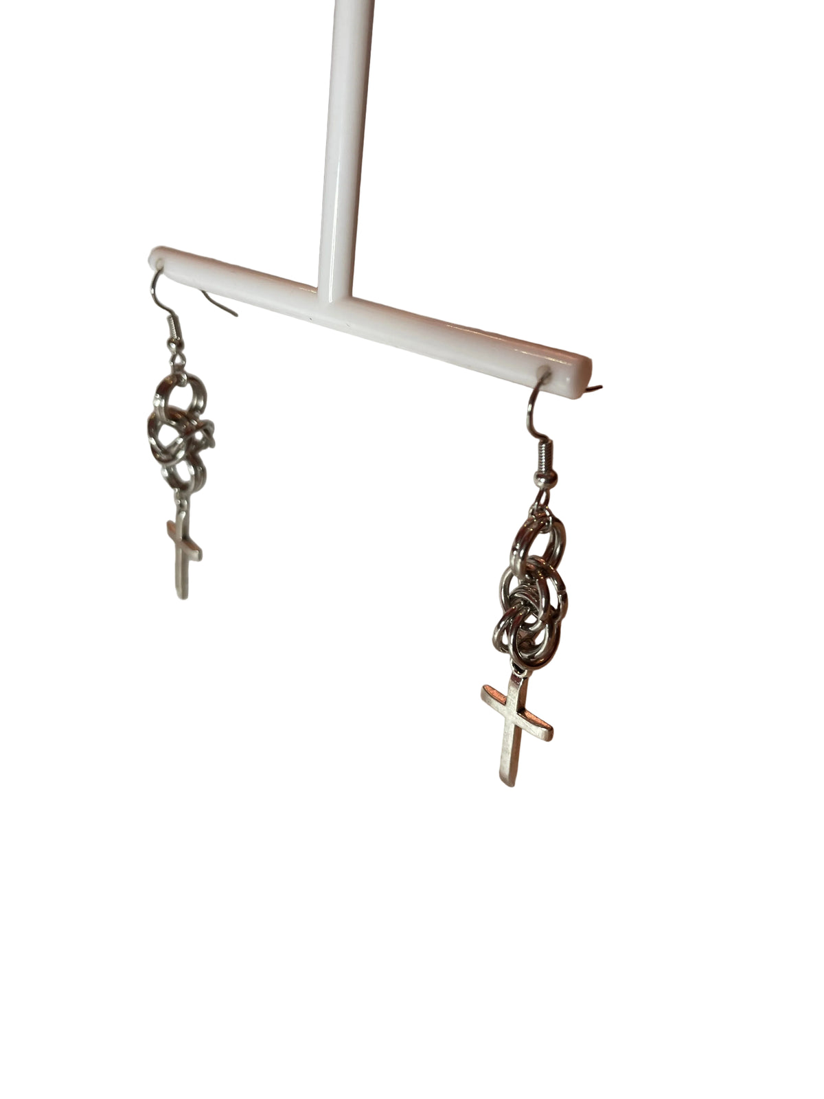 A close-up of elegant stainless steel chain mail earrings featuring a bold cross detail, hanging gracefully against a neutral backdrop. The intricate craftsmanship highlights their unique, handmade quality.