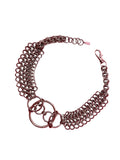 A close-up of a chain mail choker featuring intricate metal links, with bold O-rings positioned at the center. The choker rests elegantly on a neutral backdrop, highlighting its edgy, industrial design.